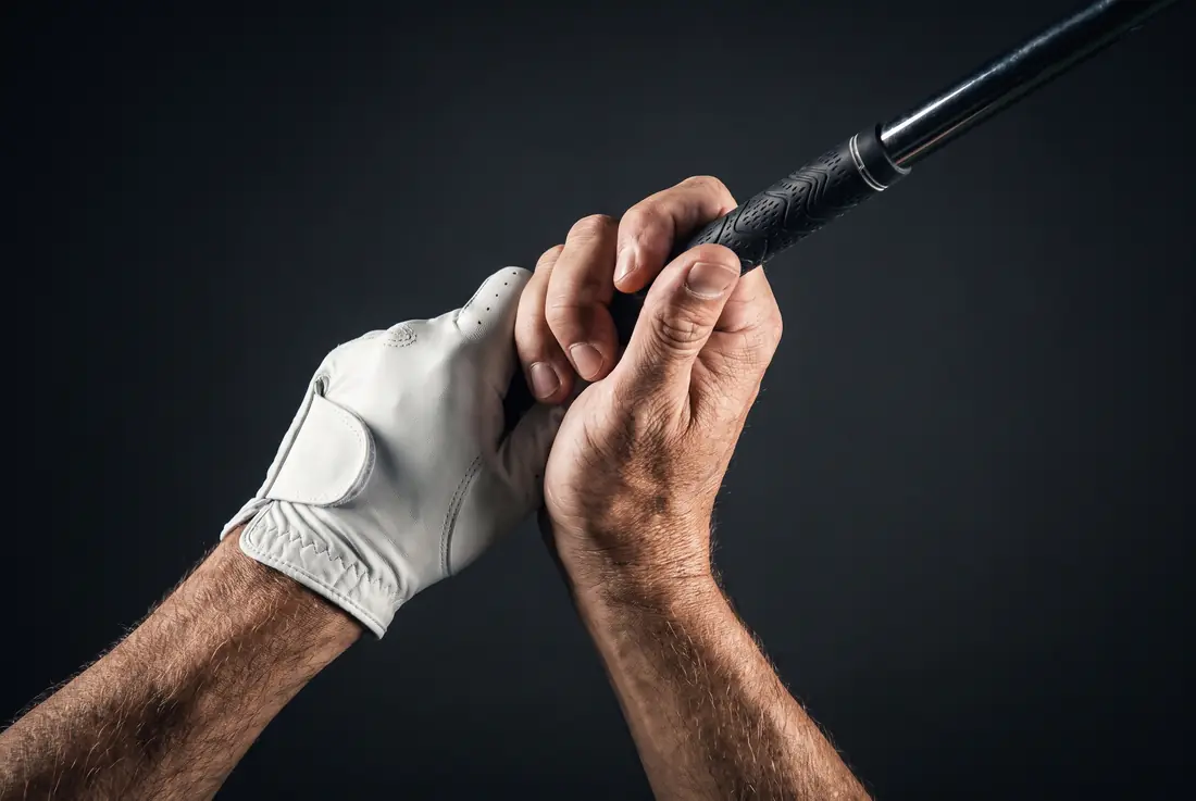 A close view of two hands gripping a club, one in a plain white glove, lit hard against a dark background.